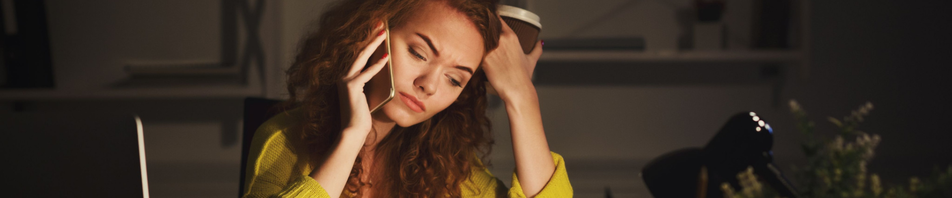 Woman looking stressed in an office on her phone holding a coffee